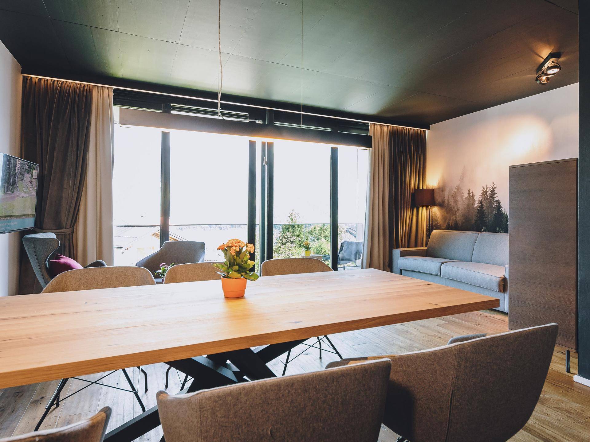 Geräumiger Wohn-Essbereich mit Holztisch, Sofa und Zugang zu einem Balkon mit weitreichender Aussicht.
