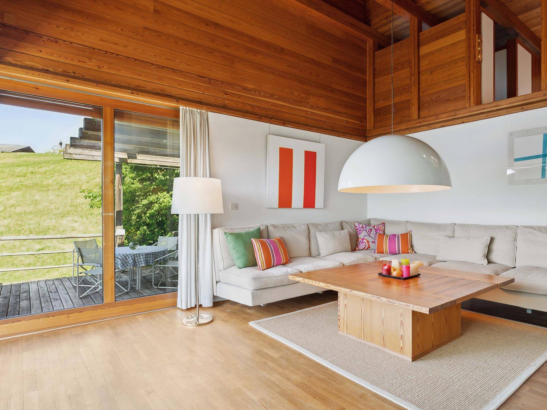 Helles Wohnzimmer mit hohen Holzdecken, großem Sofa und Zugang zu einer Außenterrasse.