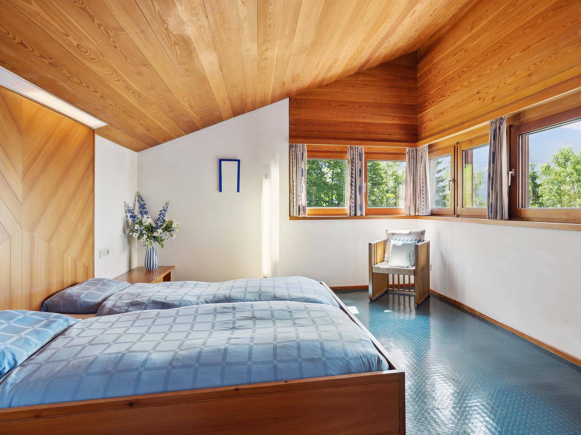 Schlafzimmer mit zwei Einzelbetten, Holzdecke und großen Fenstern mit Blick ins Grüne.