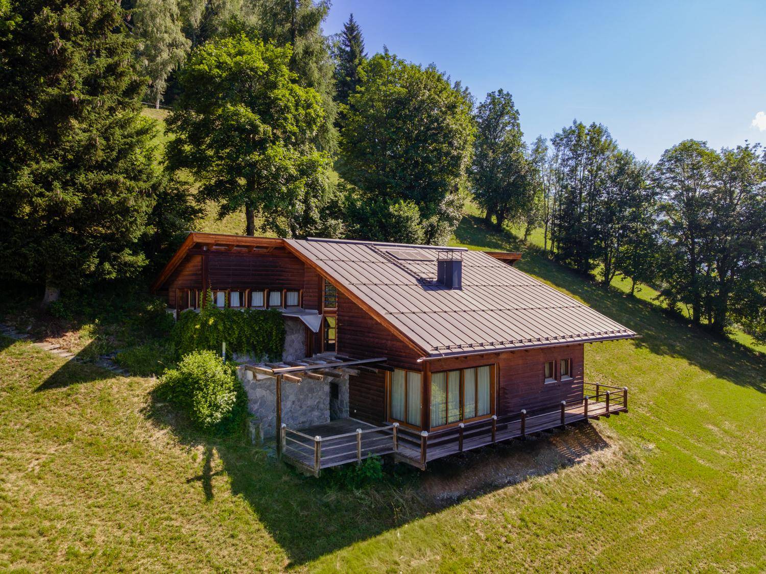 Luftaufnahme eines charmanten Holzhauses im Chalet-Stil, eingebettet in eine grüne Hügellandschaft.