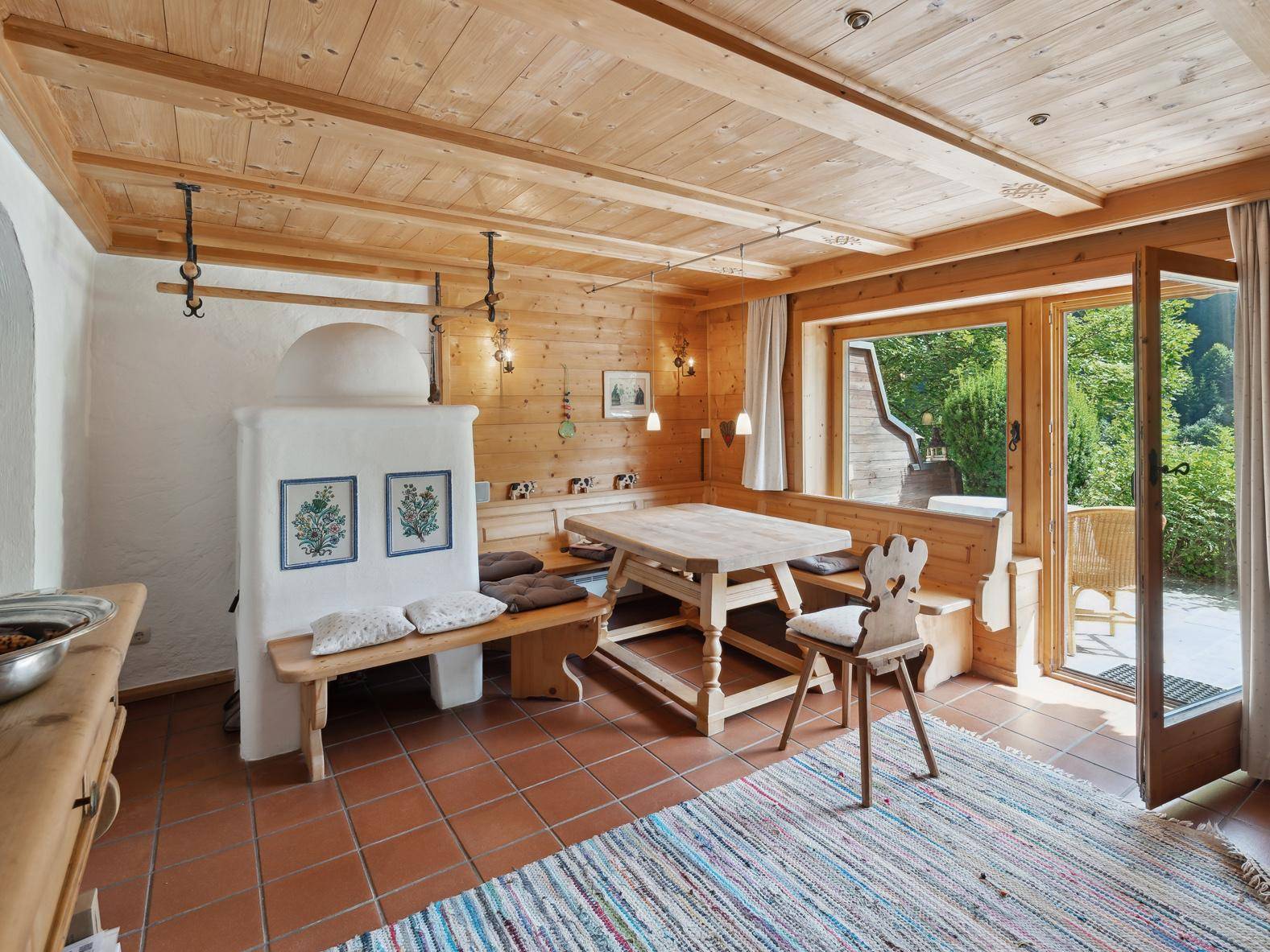 Gemütlicher Essbereich im alpinen Stil mit Kachelofen, Holztäfelung und direktem Zugang zur Terrasse.
