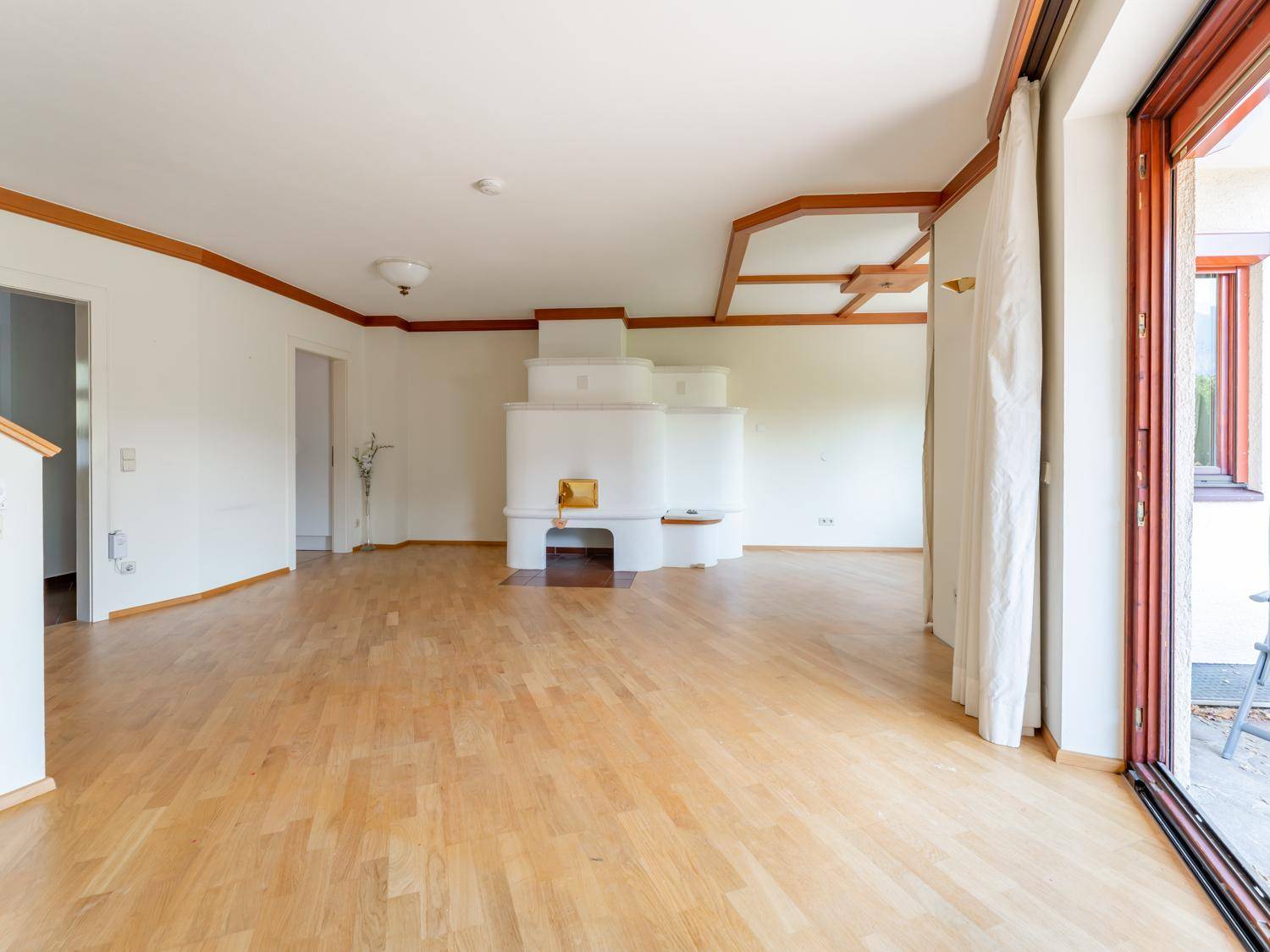 Geräumiges Wohnzimmer mit traditionellem Kachelofen, Holzbalken an der Decke und Zugang zur Terrasse.