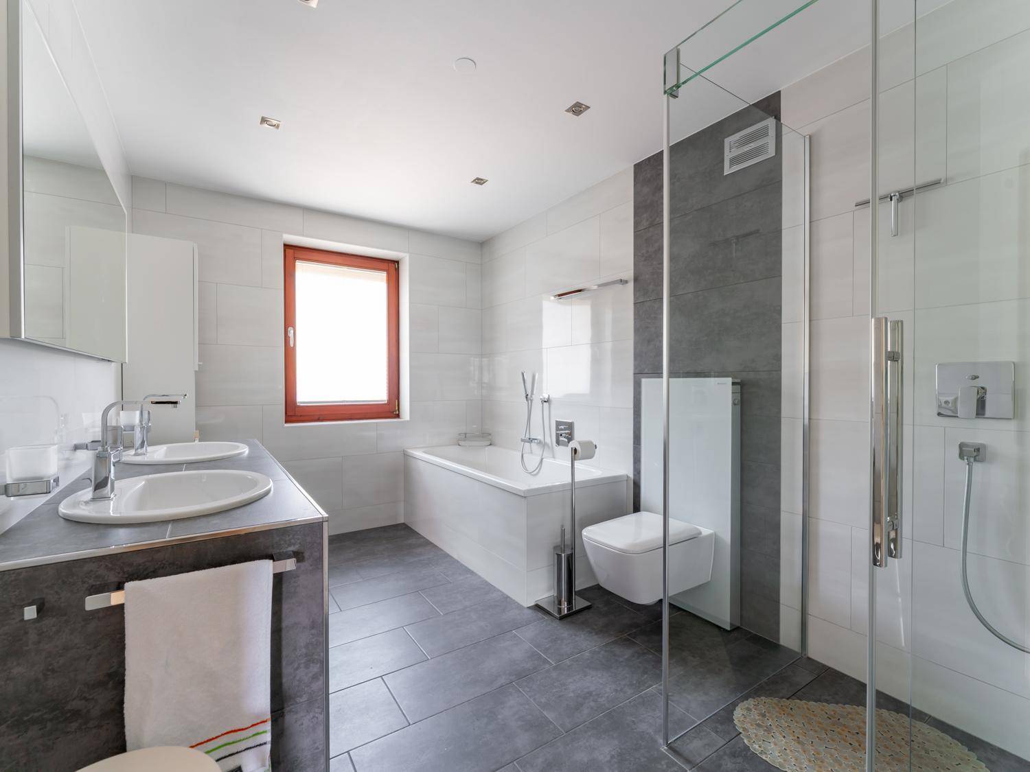 Modernes Badezimmer mit Doppelwaschbecken, Badewanne, großer begehbarer Dusche und Fenster.