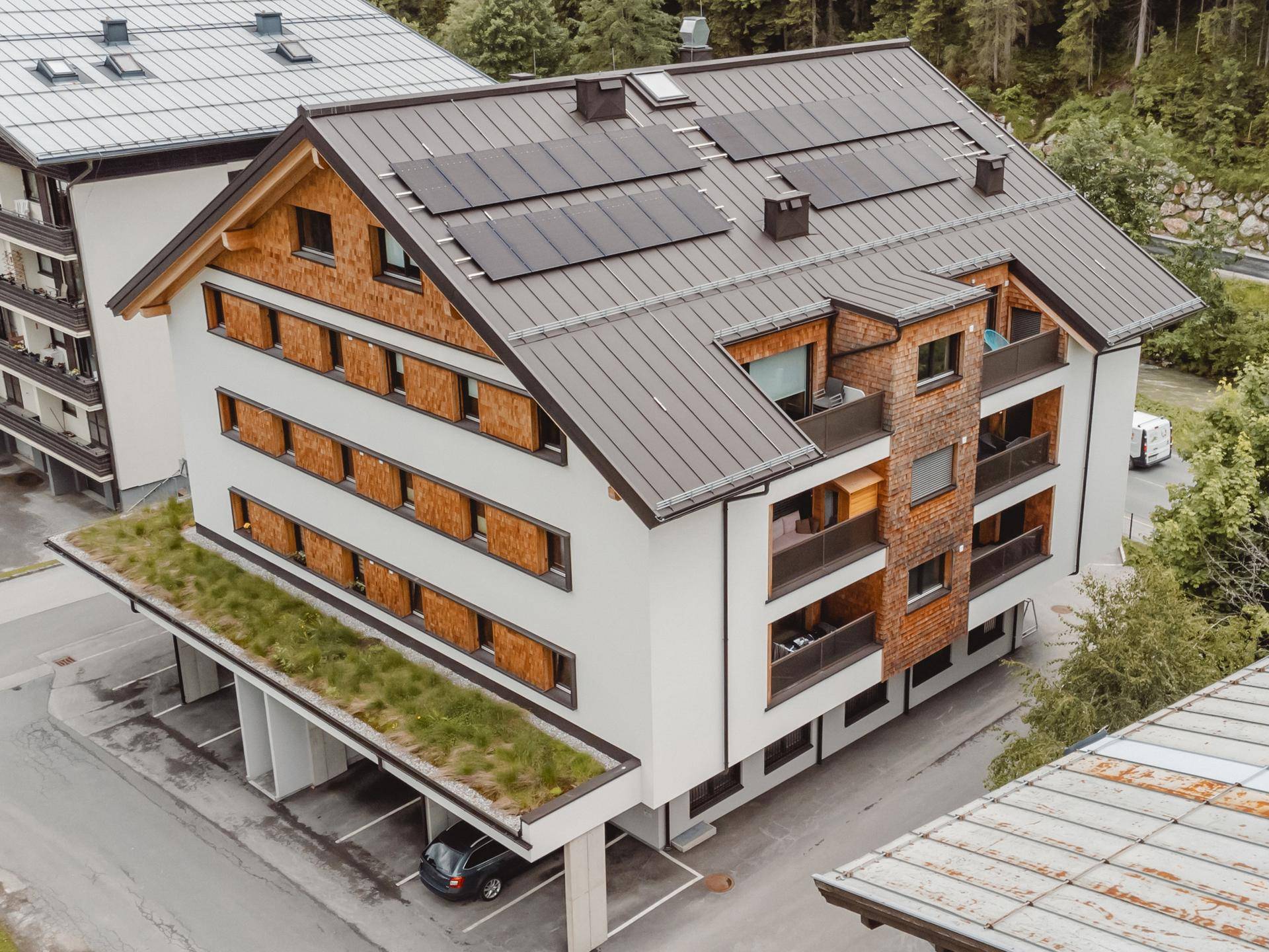 Modernes Mehrfamilienhaus mit Solaranlage, Holzfassade, Balkonen und begrüntem Carportdach.