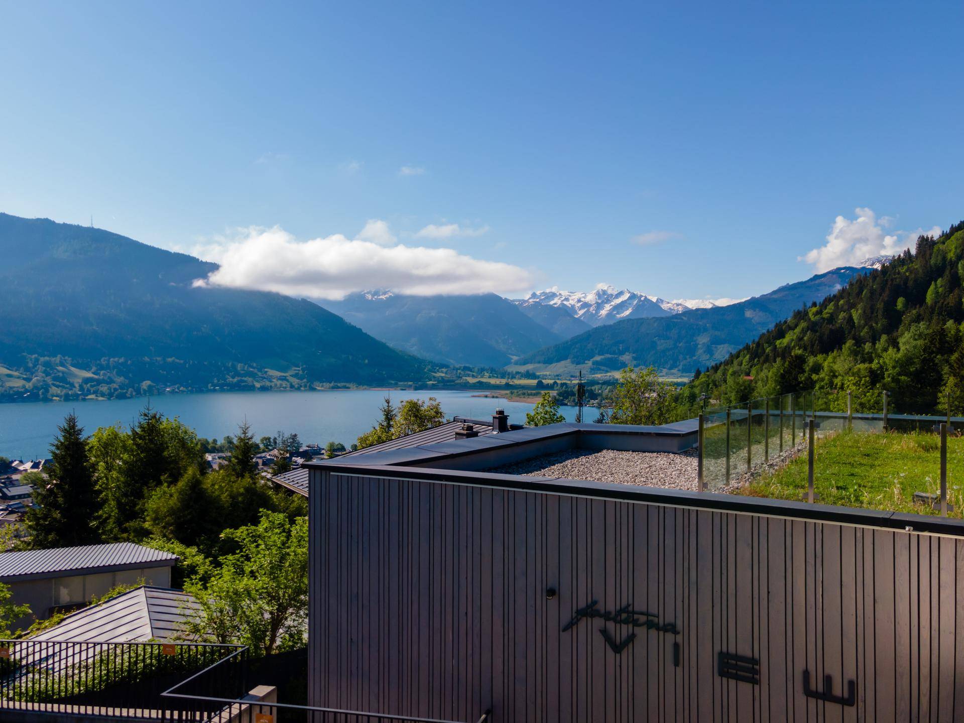 Moderne Architektur mit Flachdach und weitem Blick auf den See und die umliegenden Berge unter blauem Himmel.