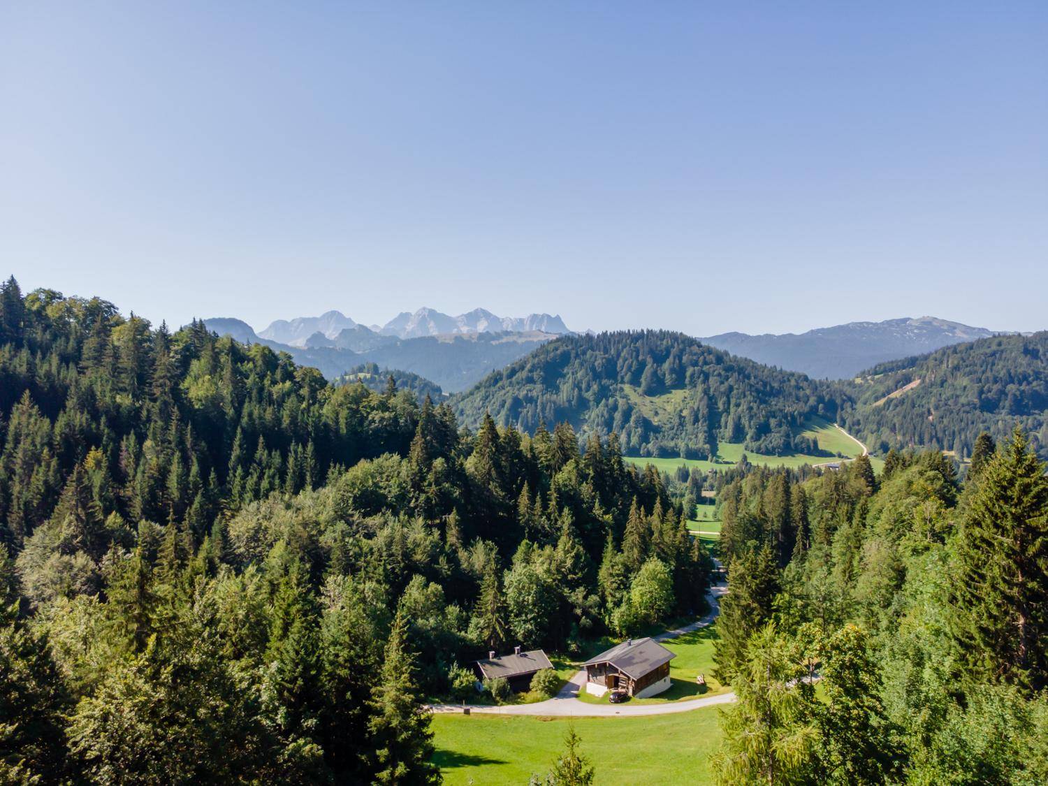 Weitläufige Berglandschaft mit dichten Wäldern und vereinzelten Häusern unter klarem Himmel.