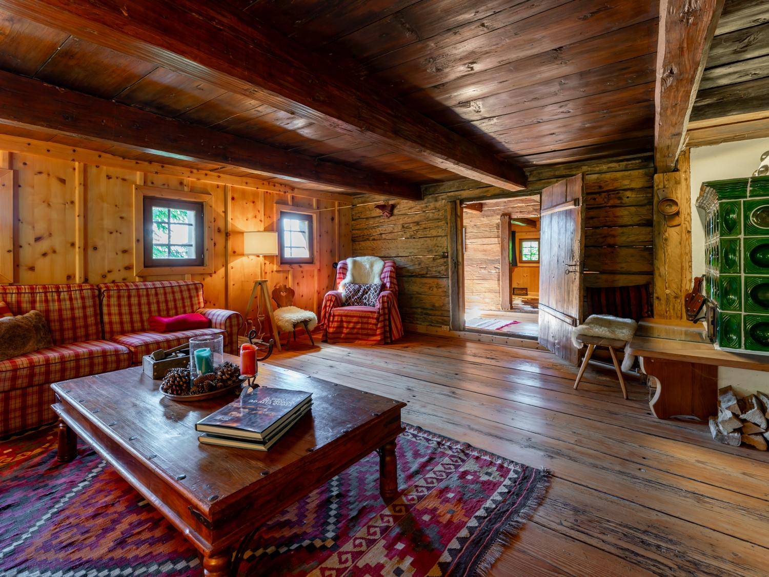 Gemütliches Wohnzimmer im alpinen Stil mit Holzböden, Kachelofen und bequemen karierten Sofas.