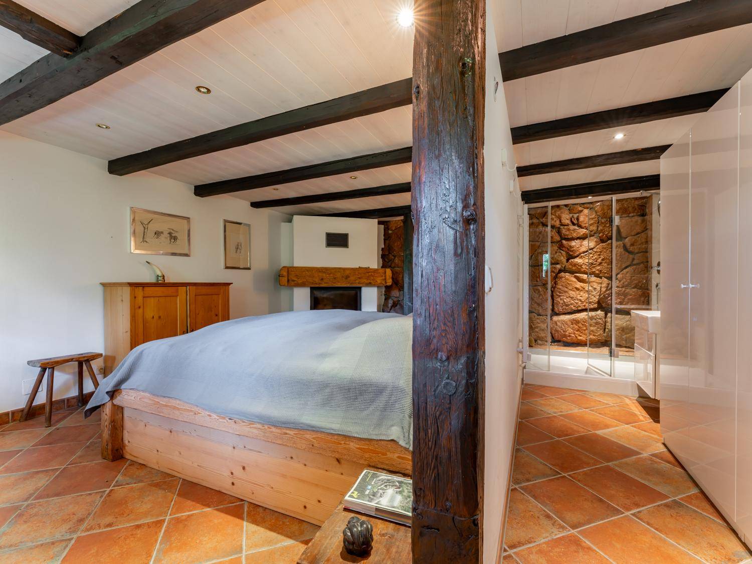Schlafzimmer im Landhausstil mit Holzbett, freiliegenden Balken und integrierter Dusche mit Steinwand.