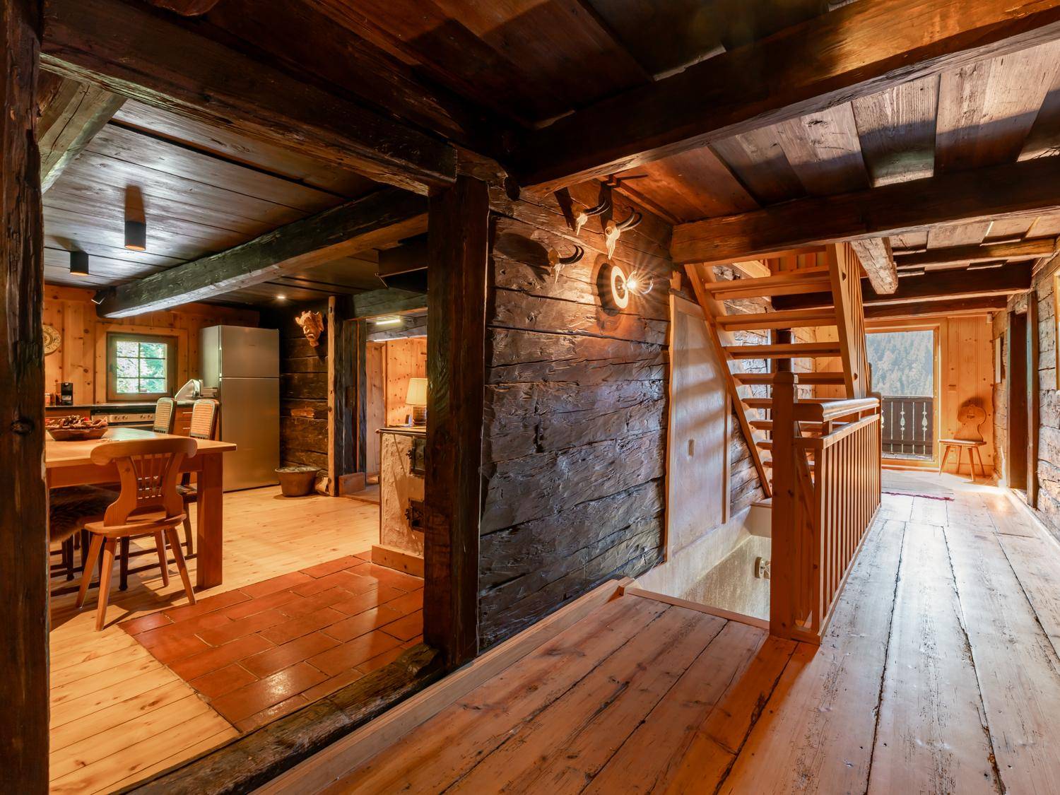Rustikaler Eingangsbereich mit Holztreppe, Holzbalken und Zugang zur traditionellen Küche.