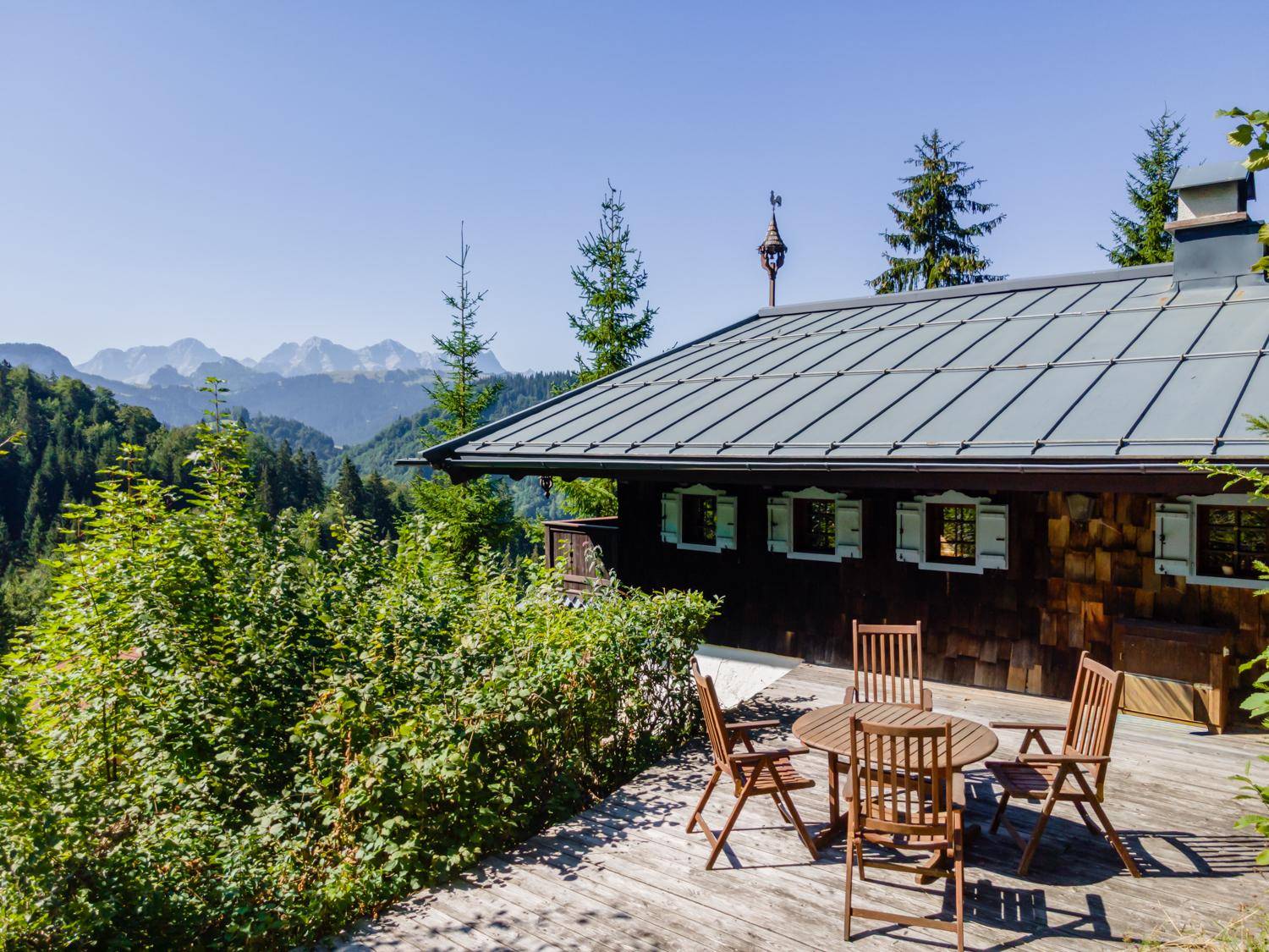 Große Holzterrasse mit Gartenmöbeln und atemberaubendem Panoramablick auf die umliegenden Berge.