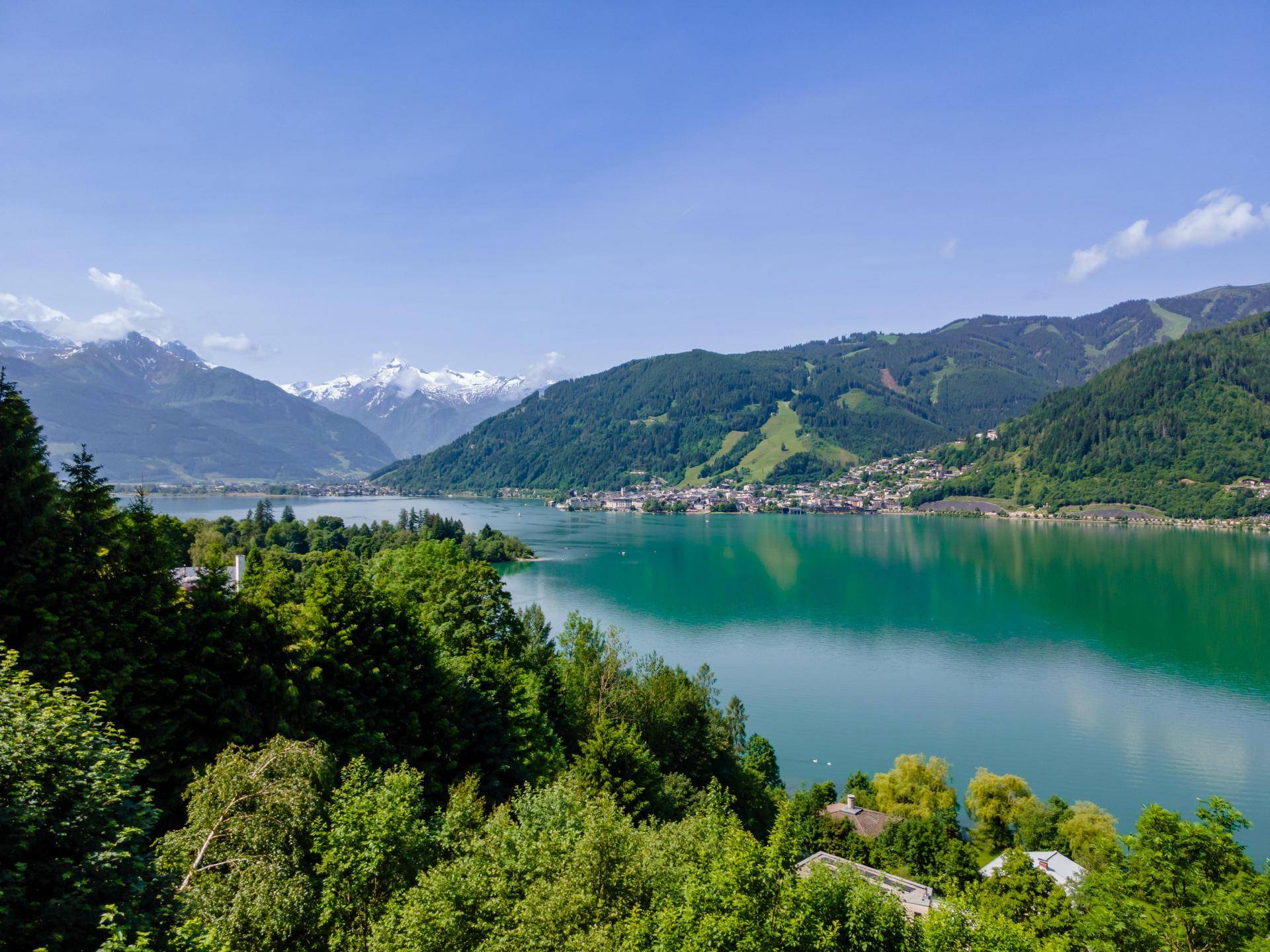 Malerischer Blick auf einen türkisfarbenen See, umgeben von grünen Bergen und einer Stadt am Ufer.