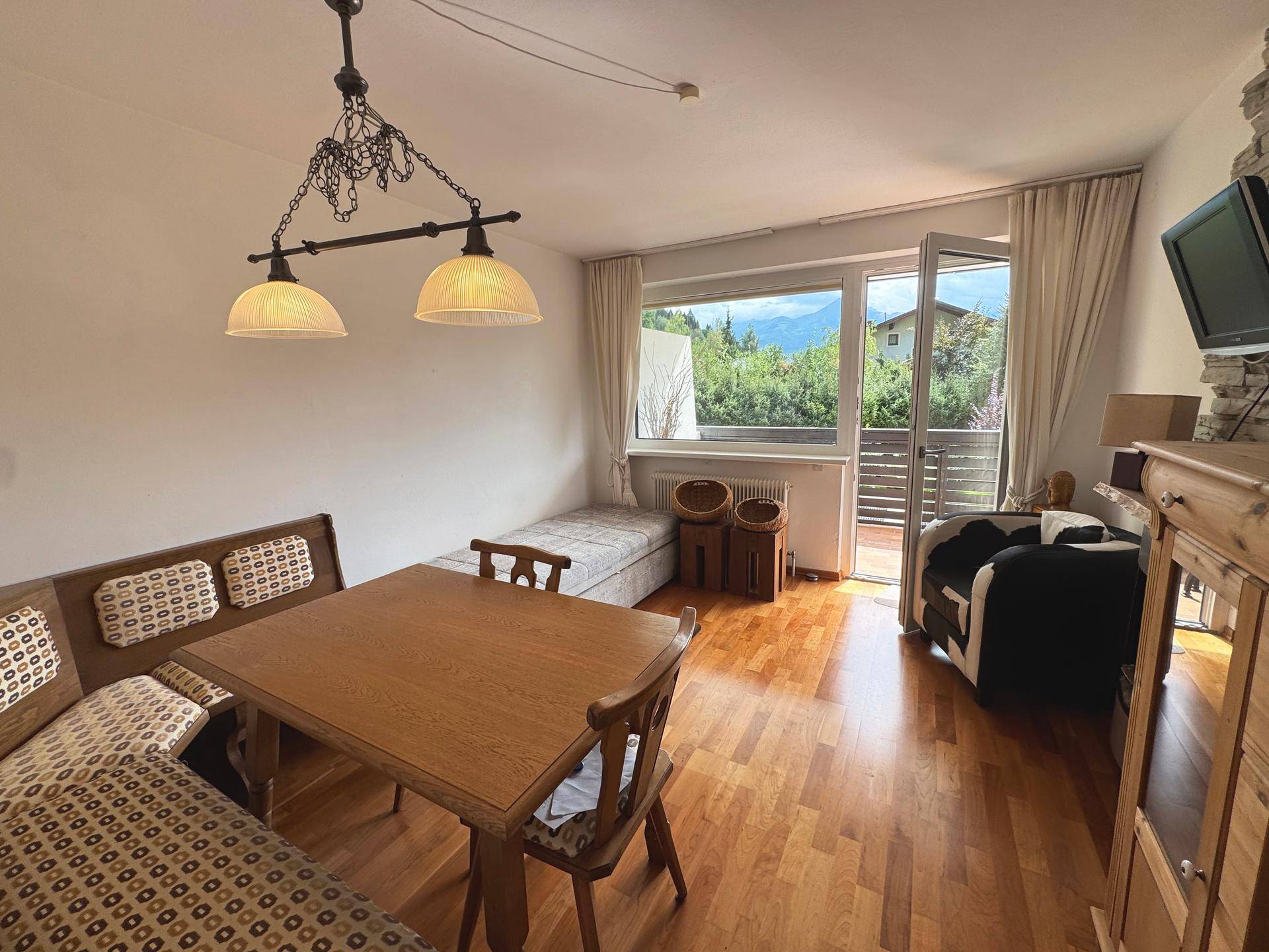 Gemütlicher Wohn-Essbereich mit Holzboden, traditioneller Sitzecke und Zugang zu einem Balkon mit Bergblick.