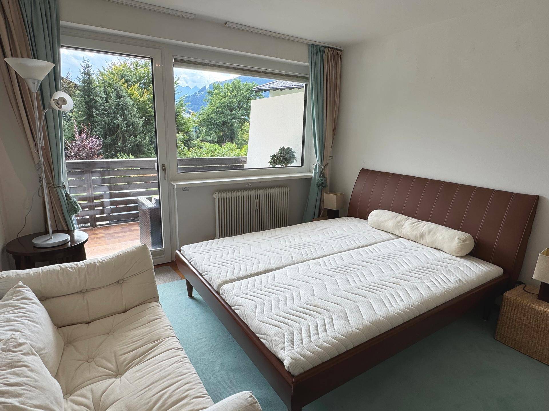 Helles Schlafzimmer mit Doppelbett, grünem Teppich und direktem Zugang zu einem Balkon mit Bergblick.