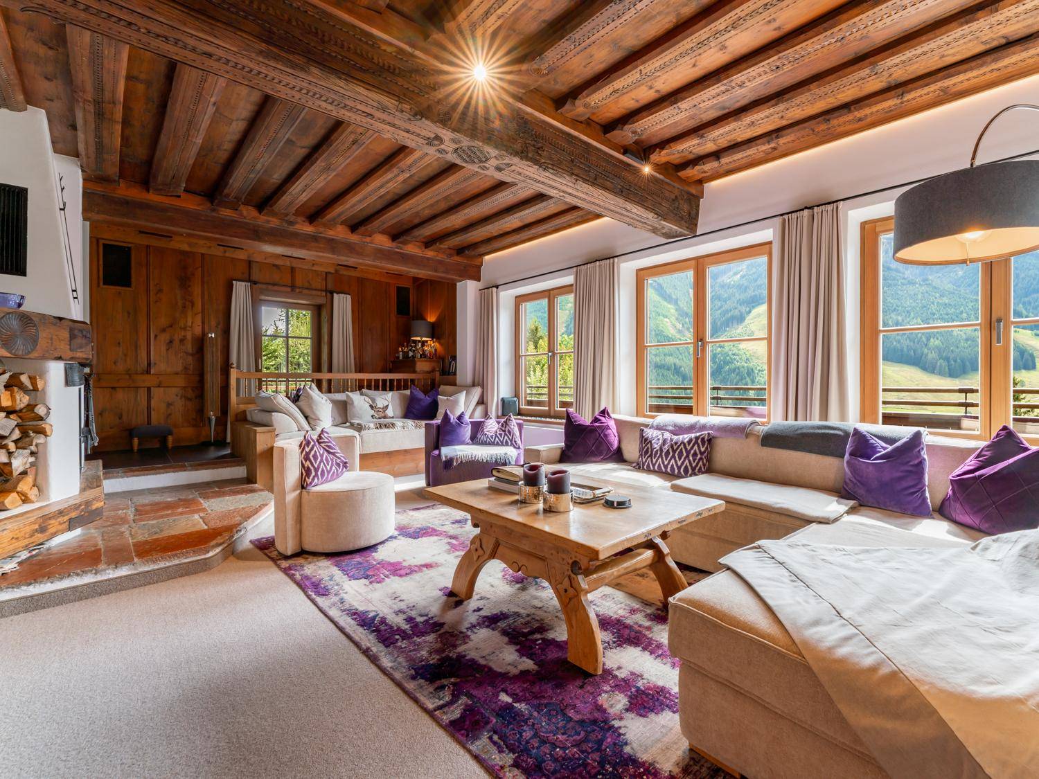 Rustikales Wohnzimmer im alpinen Stil mit Holzbalkendecke, Kamin und Panoramablick auf die Berge.