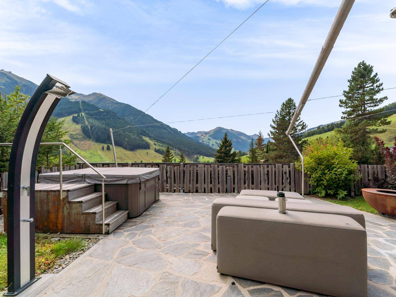 Großzügige Terrasse mit Whirlpool, Außendusche und bequemen Lounge-Möbeln vor Bergkulisse.