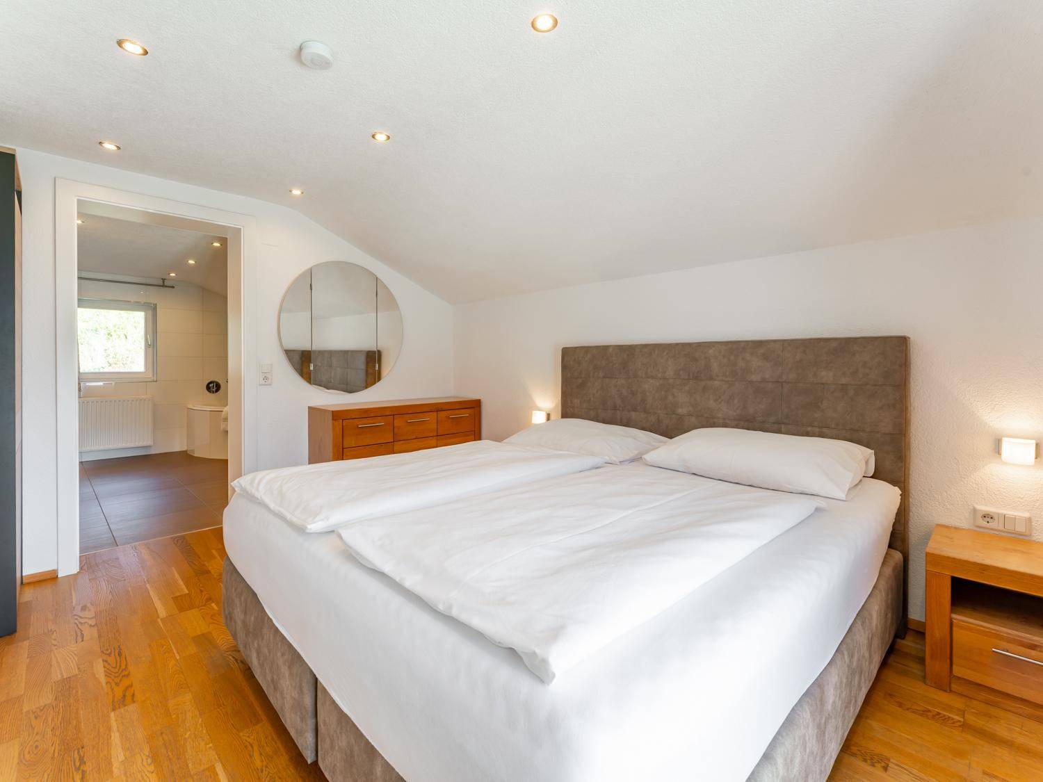 Gemütliches Schlafzimmer mit Doppelbett, Holzboden und Zugang zu einem angrenzenden Badezimmer.