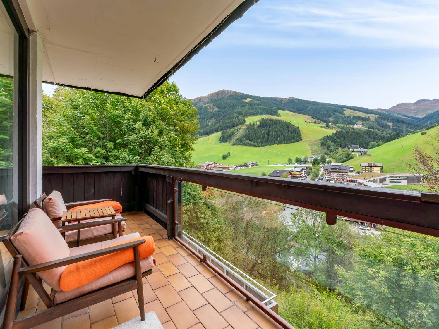 Geräumiger Balkon mit Fliesenboden, Sitzgelegenheiten und einem weiten Blick auf die grüne Berglandschaft.