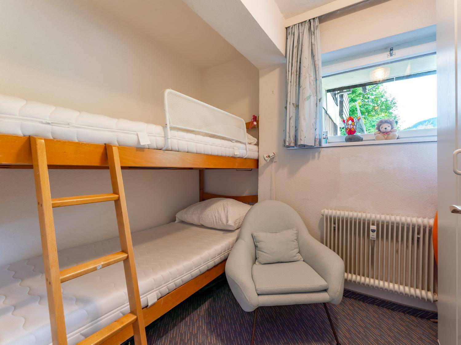 Kinderzimmer mit Etagenbett, einem kleinen Sessel und einem Fenster, ideal für Gäste oder Kinder.