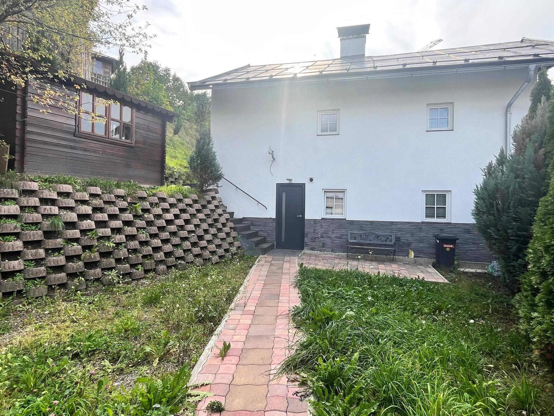 Rückseite des Hauses mit gepflastertem Weg, Rasenfläche und einer gestuften Stützmauer im Garten.