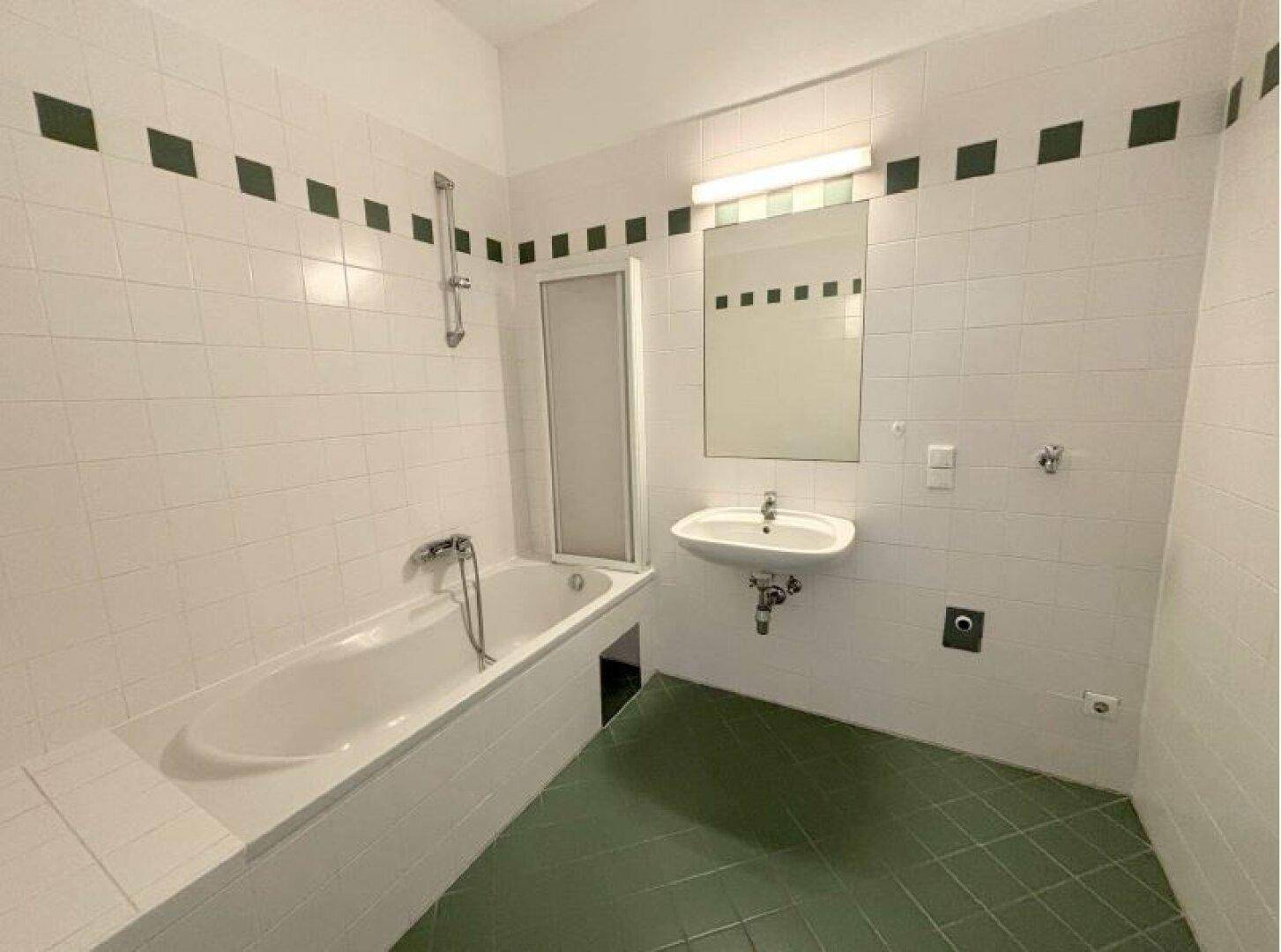 Badezimmer mit Badewanne, Duschvorrichtung, Waschbecken und weiß-grünen Fliesen.