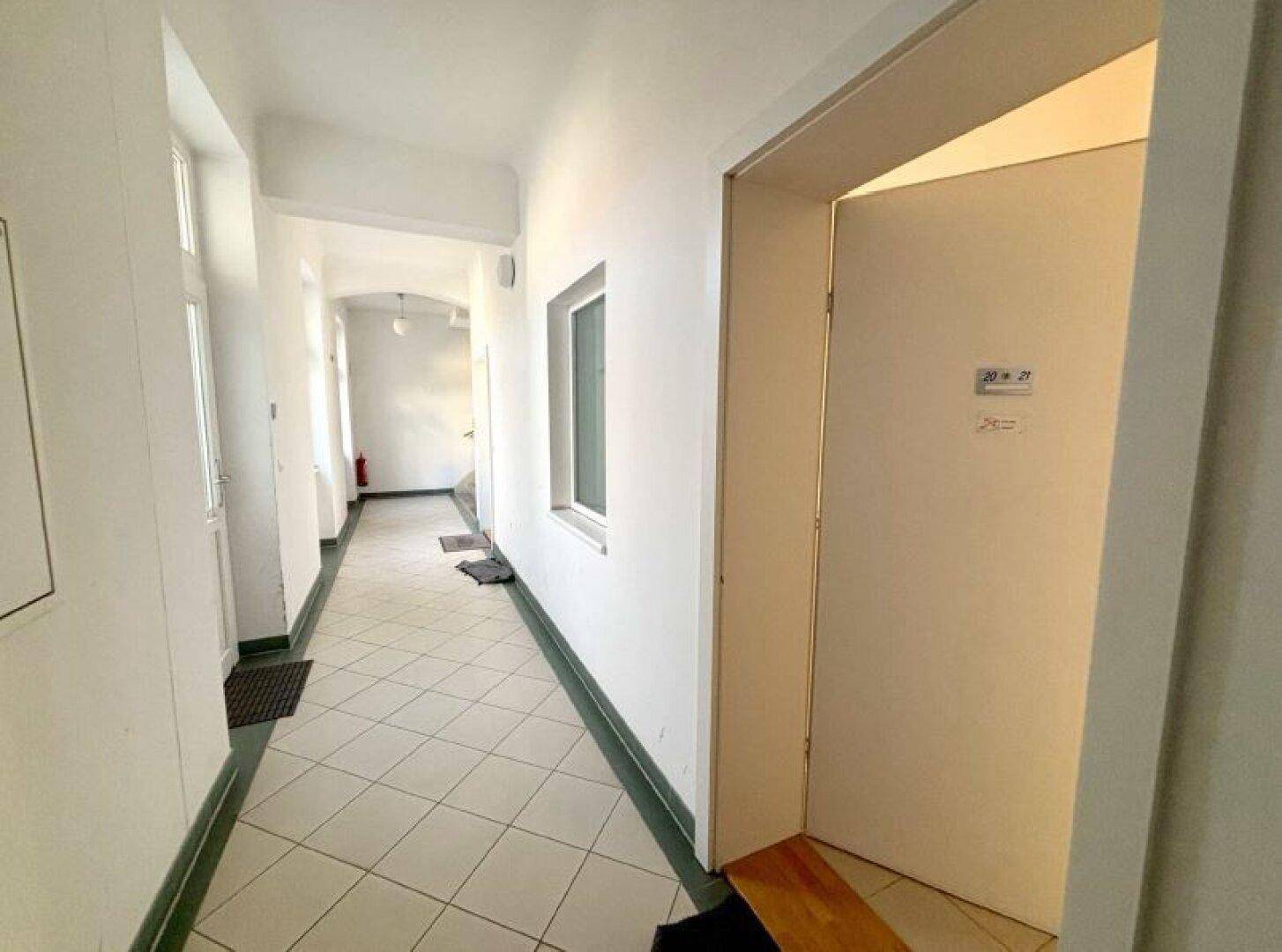 Langer, heller Flur mit weiß gefliestem Boden und mehreren Türen, der zu den verschiedenen Räumen führt.
