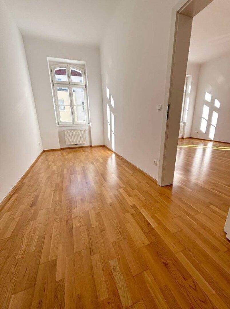 Lichtdurchfluteter Raum mit hellem Parkettboden und weiß gestrichenen Wänden, ideal für Wohn- oder Schlafzimmer.