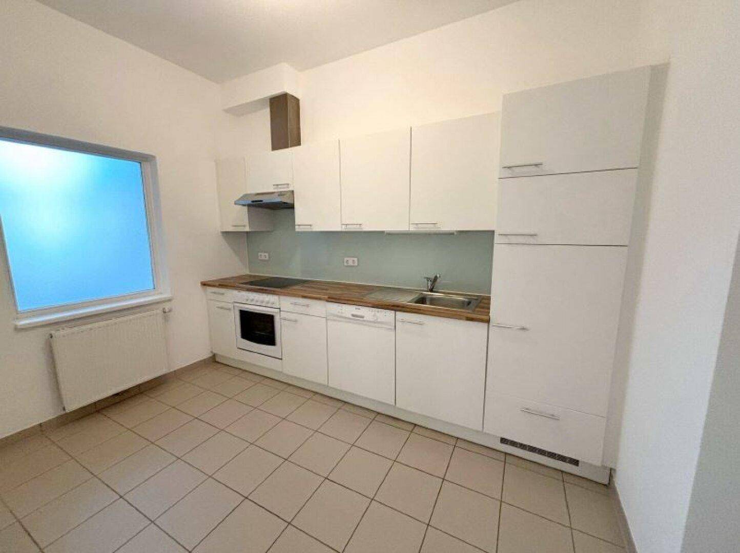 Kleine, funktionale Küche mit weißen Schränken, Holzarbeitsplatte und gefliestem Boden.