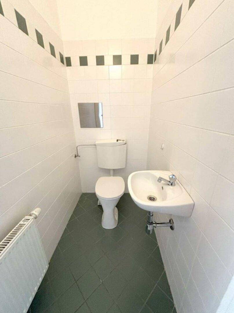 Kleines Gäste-WC mit weißen Wandfliesen, grünem Boden und einem Waschbecken.