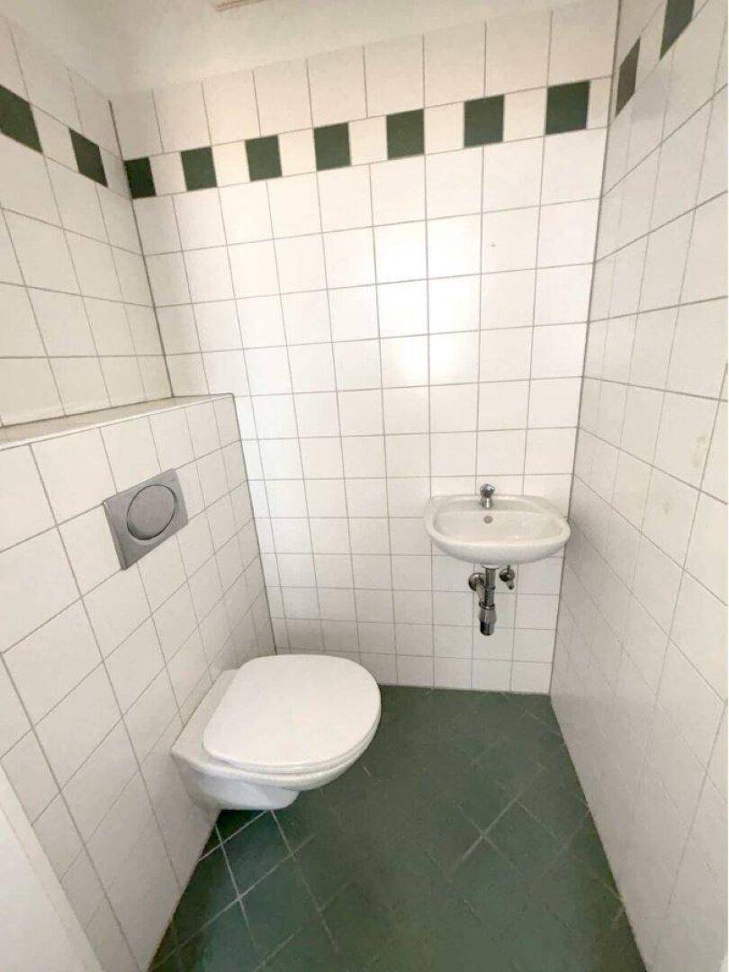 Kleines Gäste-WC mit weißen Fliesen, Wand-WC und kleinem Waschbecken in schlichtem Design.