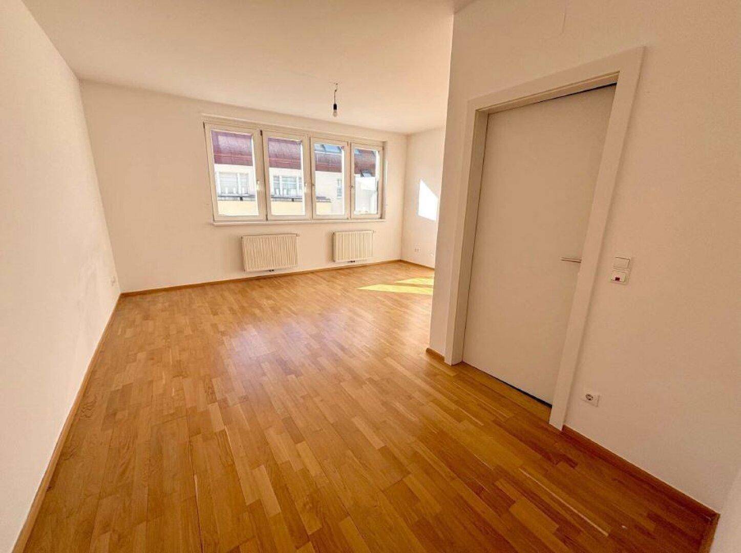 Geräumiges, helles Zimmer mit Holzparkett und großen Fenstern, ideal für individuelle Gestaltung.