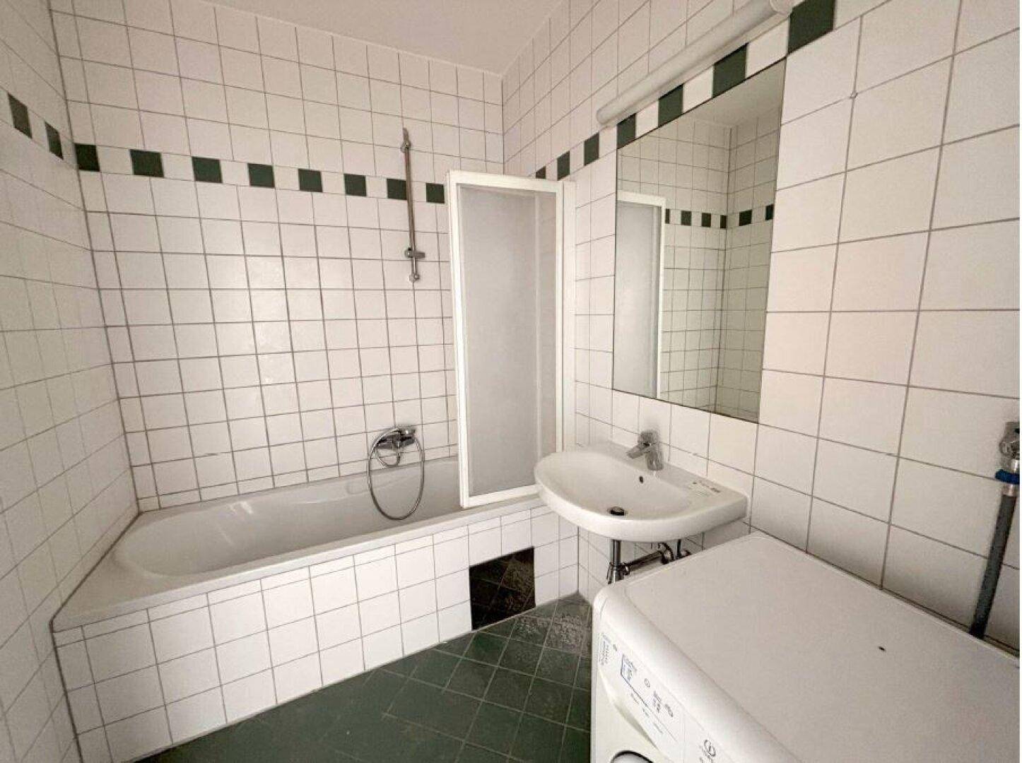 Badezimmer mit Badewanne, Dusche, Waschbecken und Waschmaschine, komplett gefliest im 80er-Jahre-Stil.
