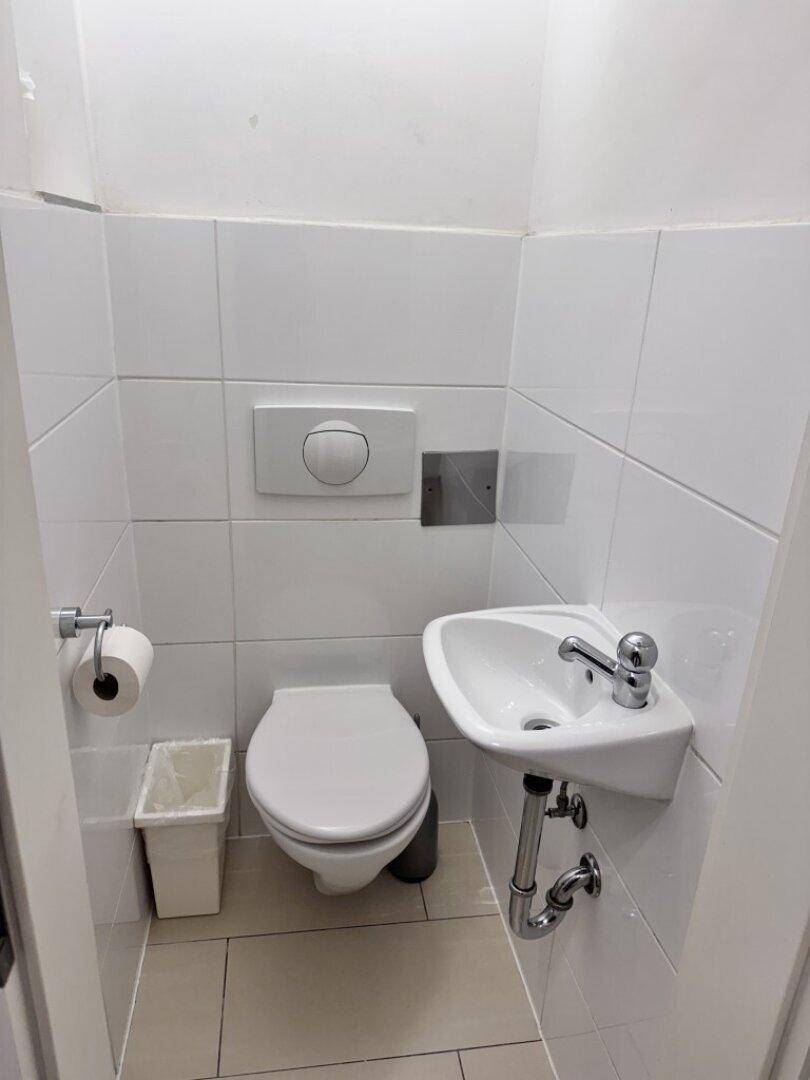 Kleines Gäste-WC mit weiß gefliesten Wänden, Toilette und Handwaschbecken.