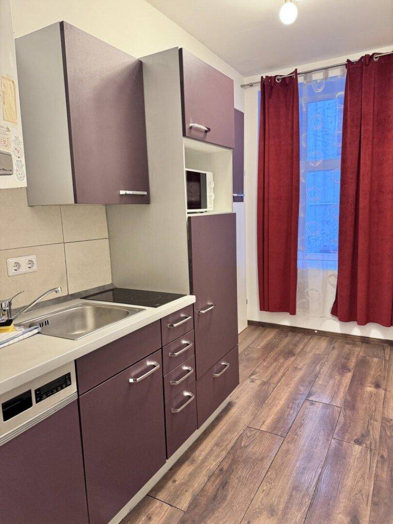 Küchenzeile mit Spüle, Kochfeld und Fenster, ausgestattet mit modernen lila Schränken.