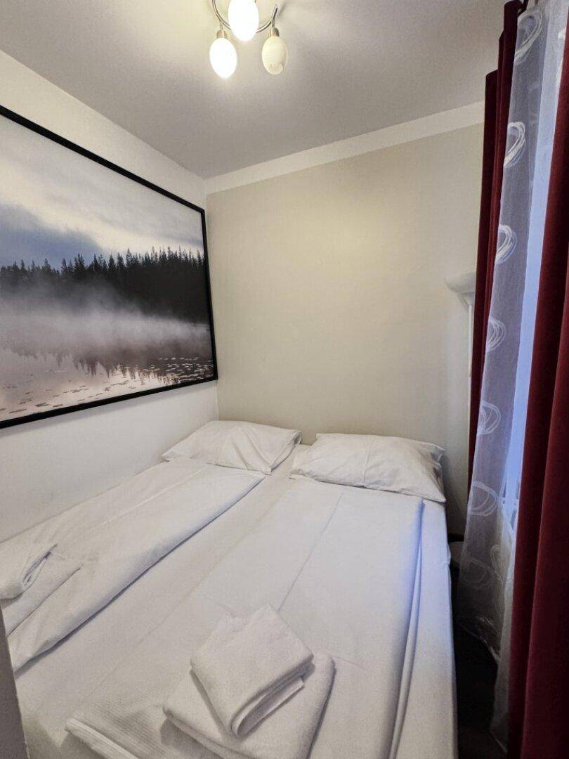 Kleines Schlafzimmer mit Doppelbett und roten Vorhängen, dekoriert mit einem Landschaftsbild.