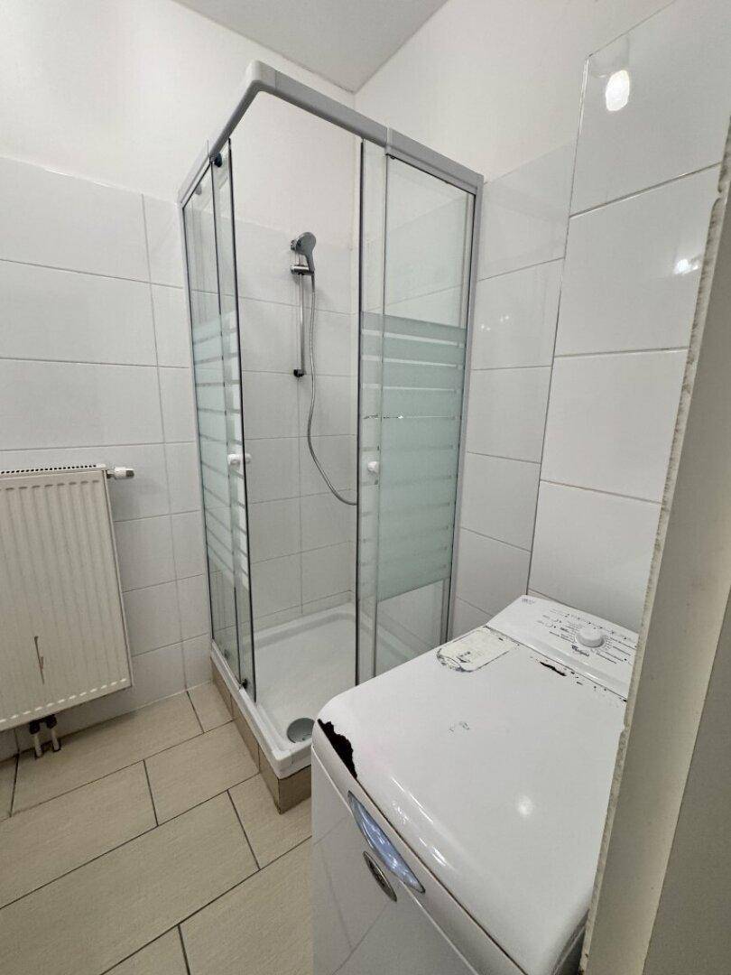 Badezimmer mit Duschkabine und Waschmaschine, hell gefliest und funktional eingerichtet.