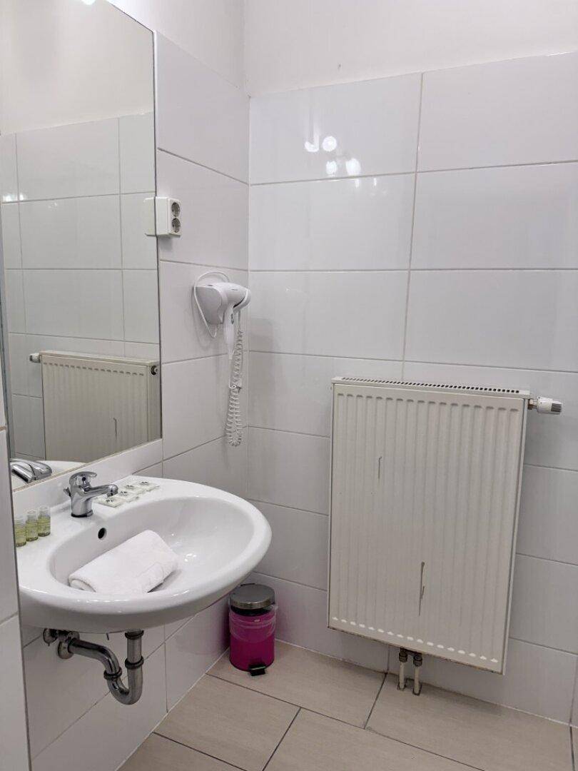 Badezimmer mit Waschbecken, großem Spiegel und Heizkörper, komplett weiß gefliest.
