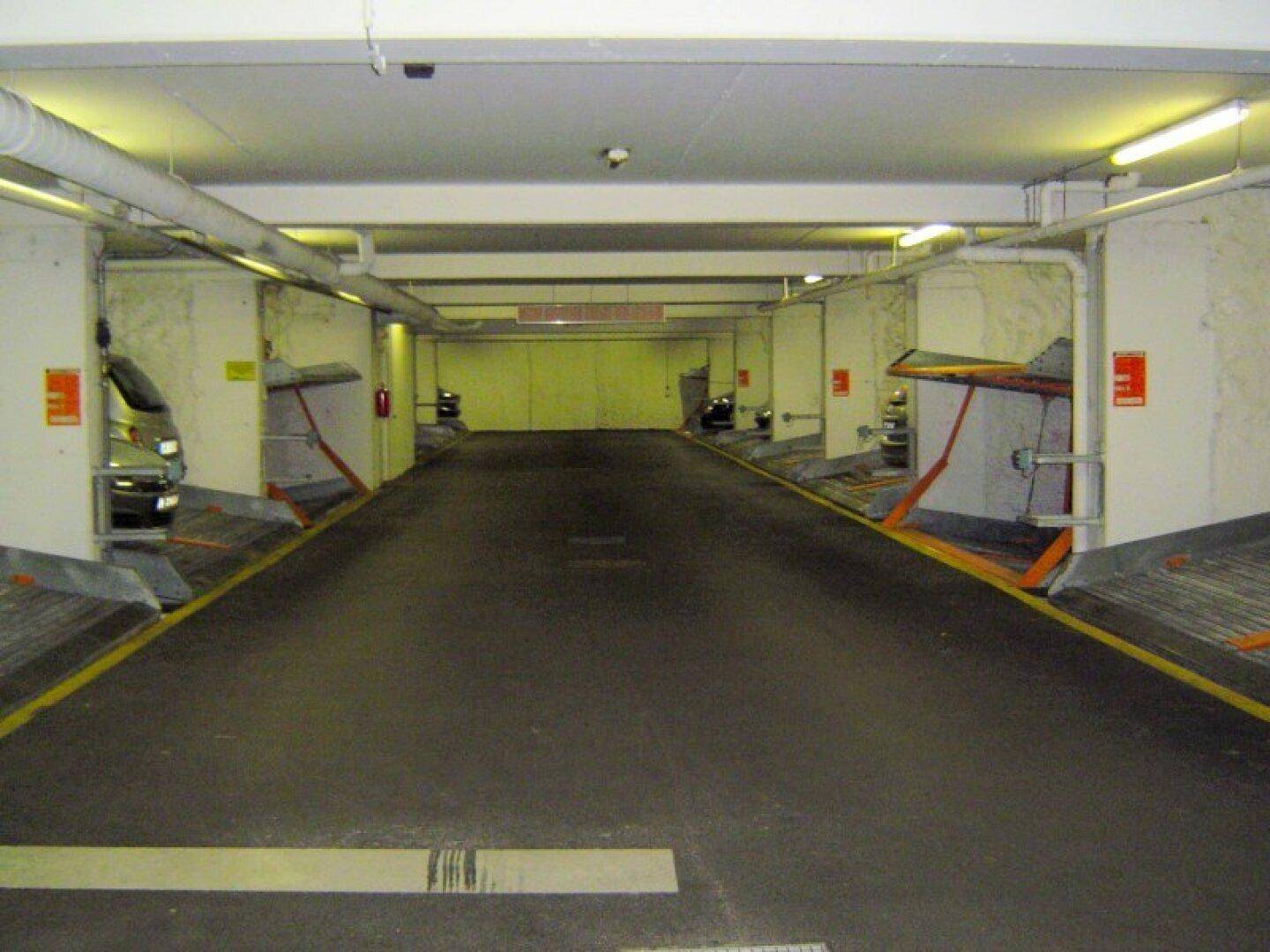 Innenansicht einer Tiefgarage mit automatischen Parkliftsystemen und heller Deckenbeleuchtung.
