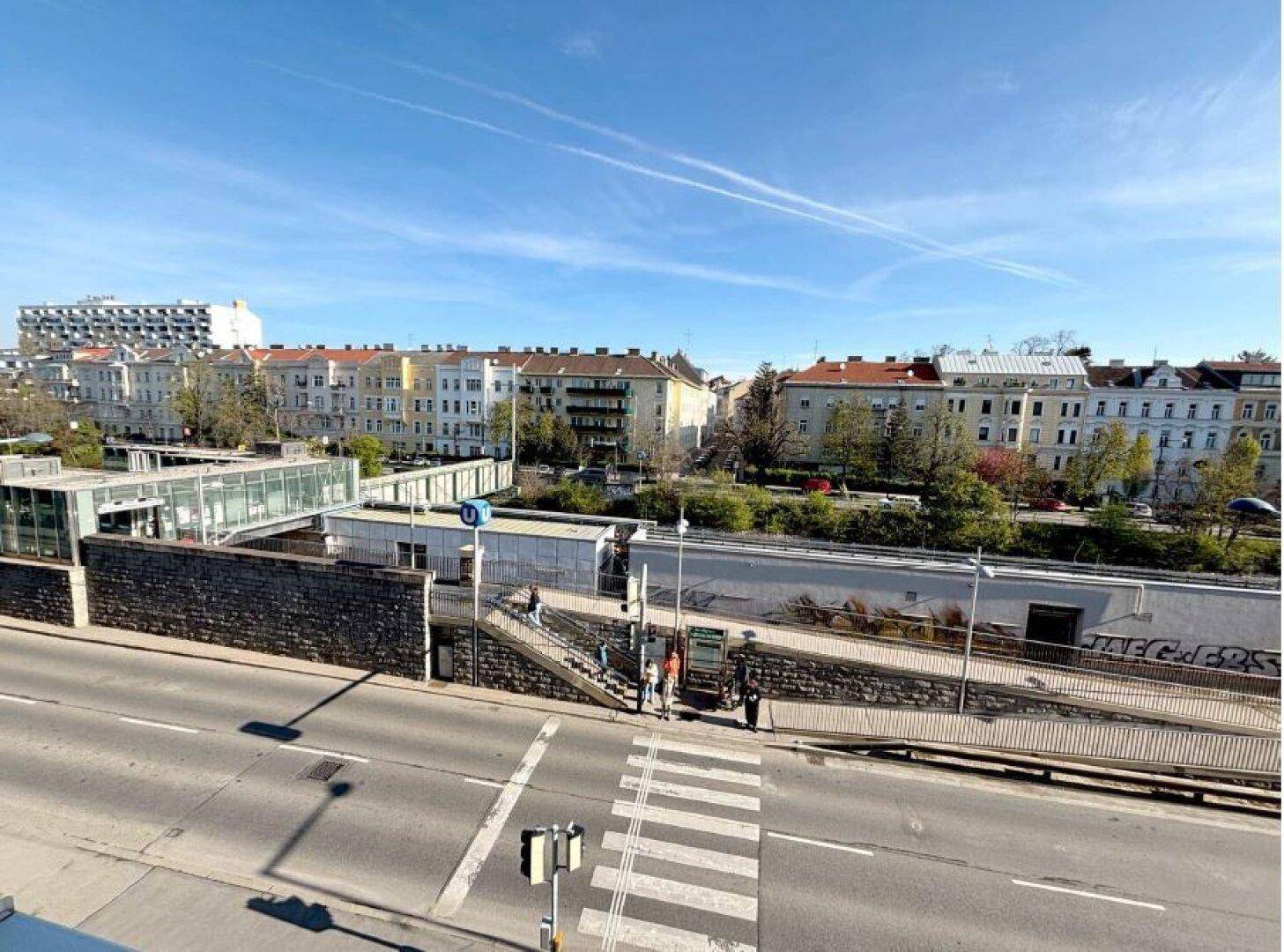 Blick aus dem Fenster auf eine belebte Straße, eine U-Bahn-Station und umliegende Stadtgebäude.