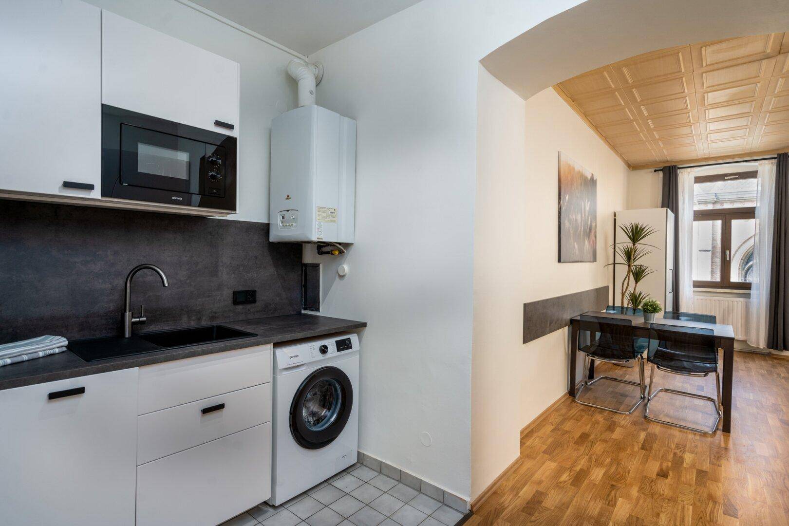Funktionale Küchenzeile mit Waschmaschine, Mikrowelle und Stauraum in einem Studio-Apartment.