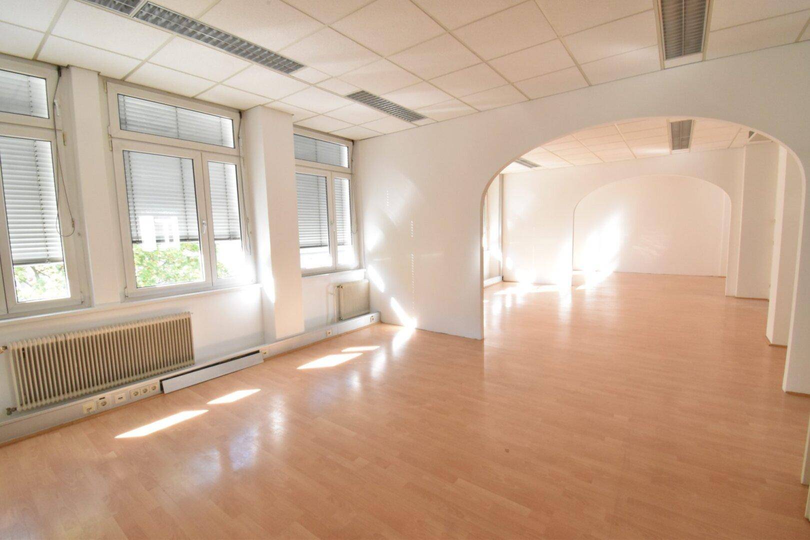 Großzügiger Bürobereich mit Holzboden, großen Fenstern und eleganten Bögen, die eine offene Atmosphäre schaffen.
