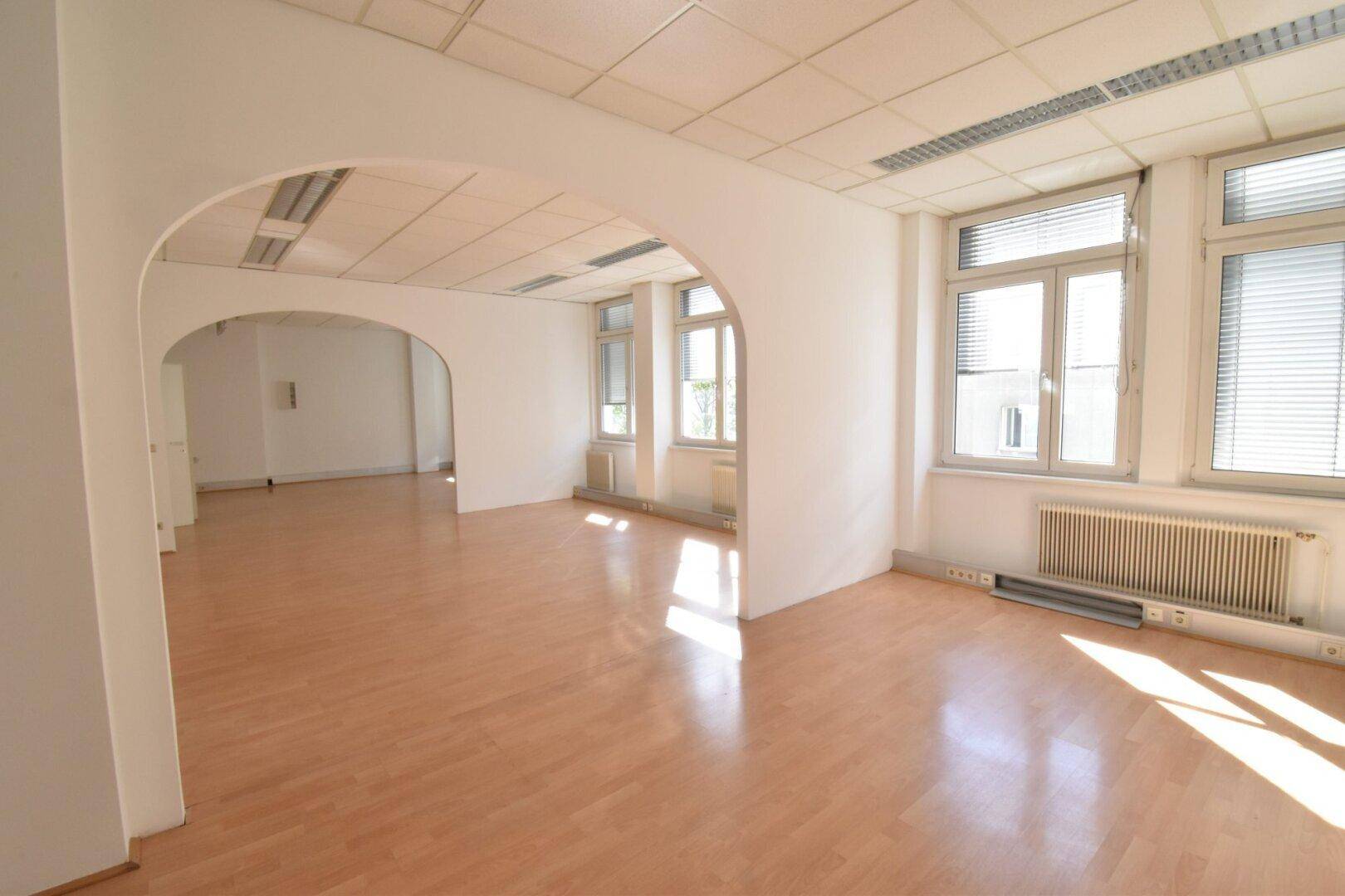 Heller Büroraum mit Holzboden und architektonischen Bögen, die verschiedene Bereiche miteinander verbinden.