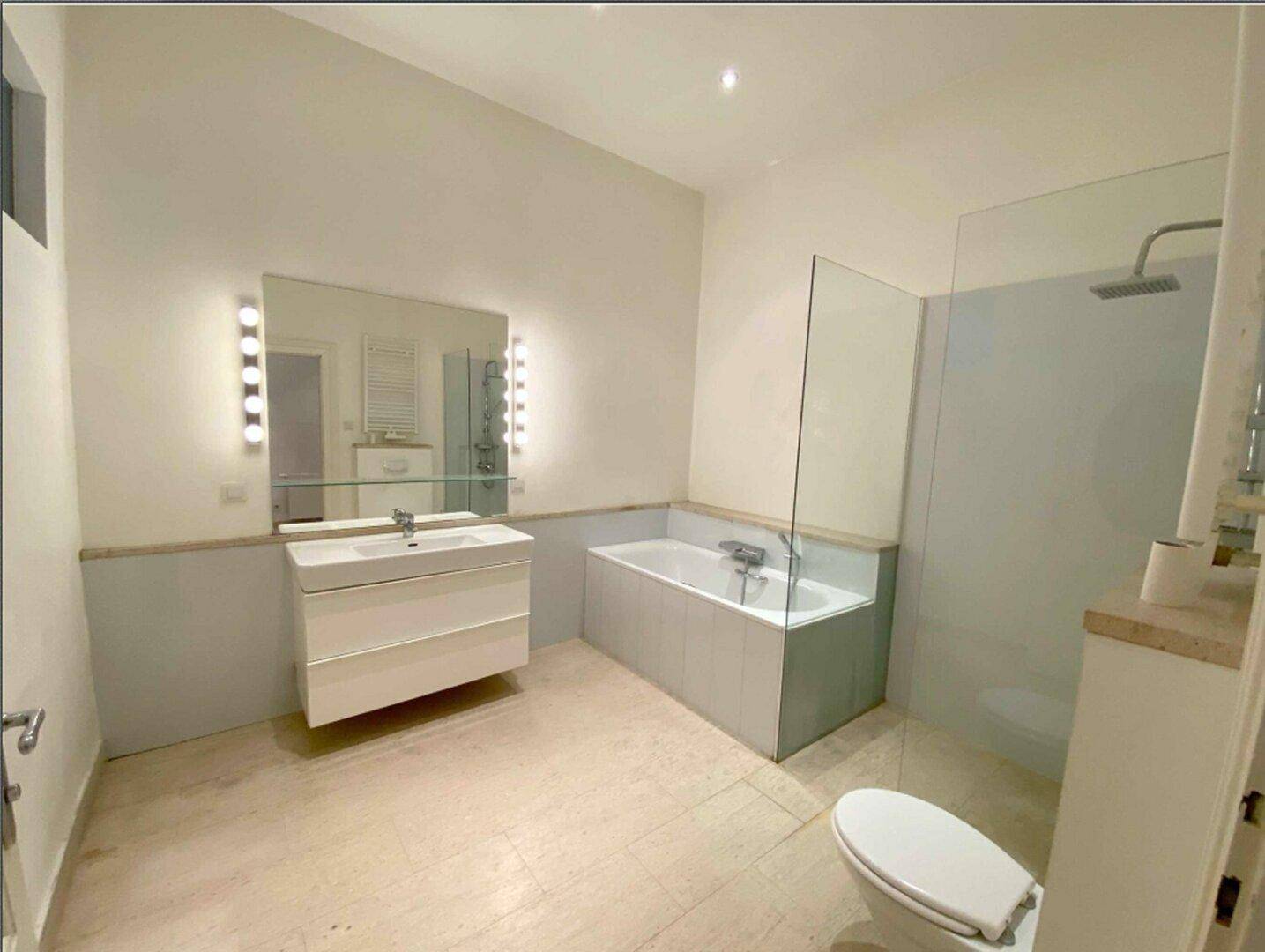 Modernes Badezimmer mit Badewanne, Duschbereich und großem Spiegel mit Beleuchtung.