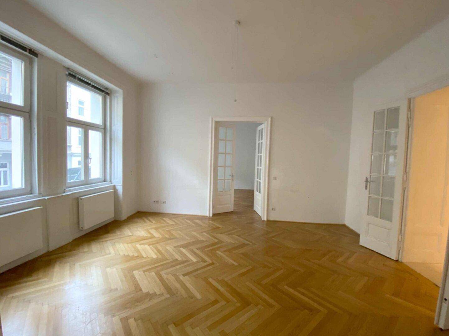 Helles Wohnzimmer mit klassischem Fischgrätparkett und Flügeltüren zu weiteren Räumen.