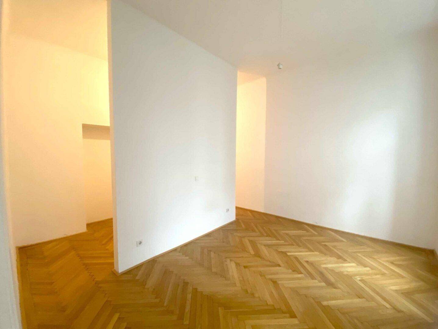 Leerer Raum mit Fischgrätparkett und weißen Wänden, bereit für die individuelle Gestaltung.