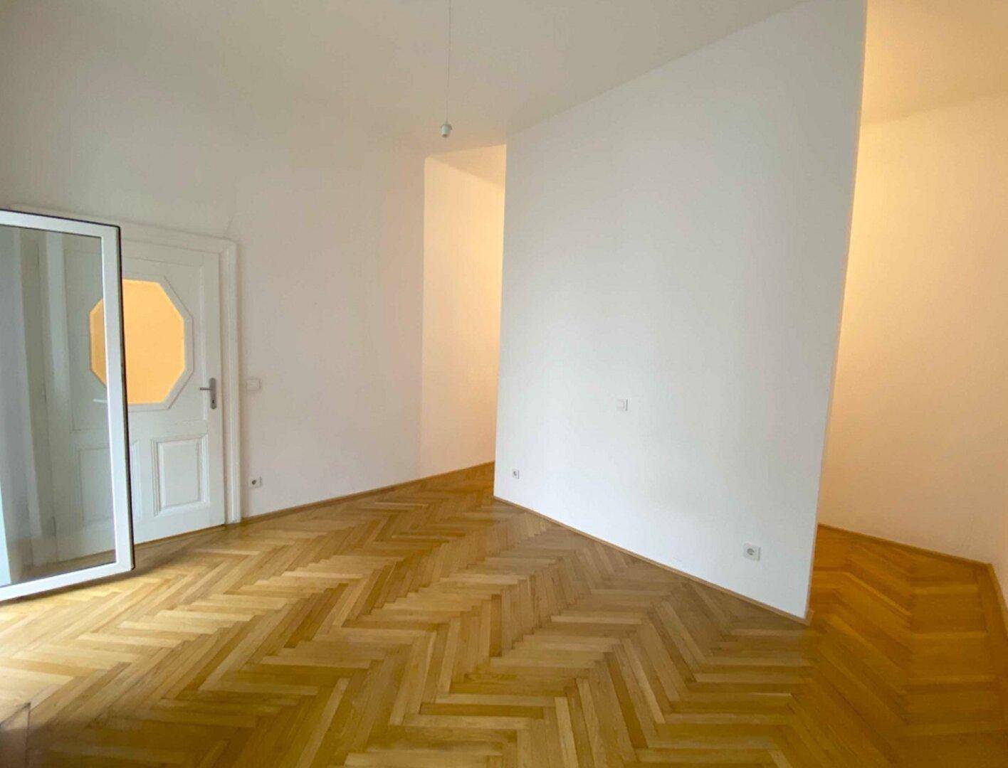 Leerer Raum mit Fischgrätparkett und weißer Trennwand, ideal für flexible Nutzung.