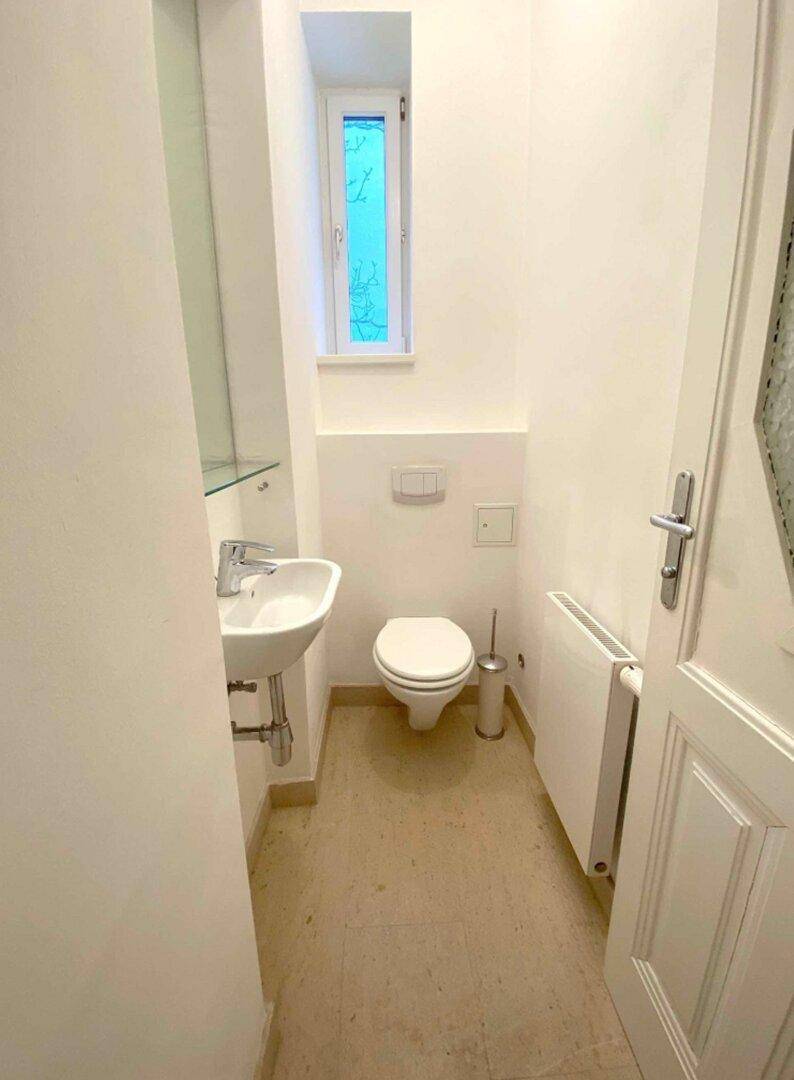 Kleines Gäste-WC mit wandhängendem WC, Waschbecken und Fenster für Tageslicht.