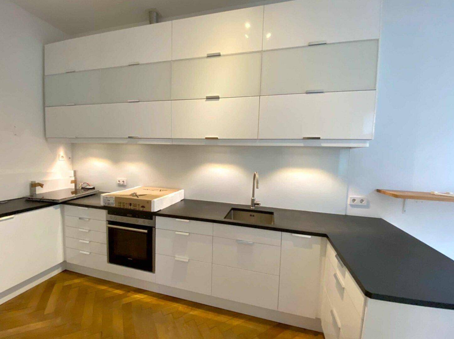 Moderne Einbauküche mit weißen Hochglanzschränken, dunkler Arbeitsplatte und integriertem Backofen.