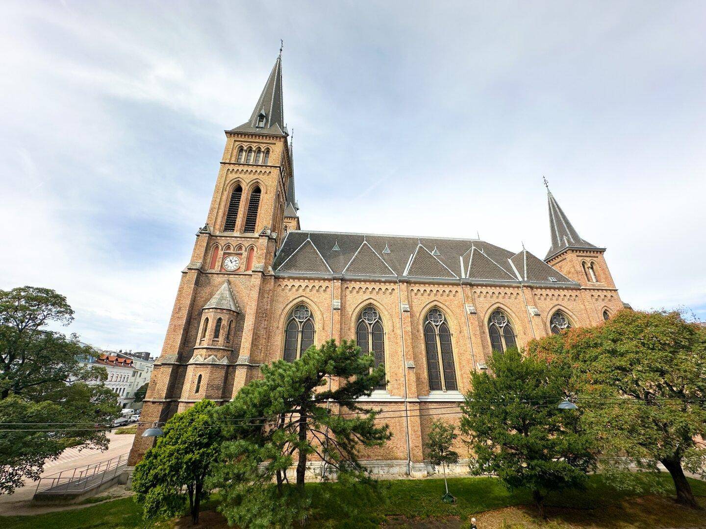 Historische Kirche mit imposanten Türmen und detailreicher Architektur unter bewölktem Himmel.