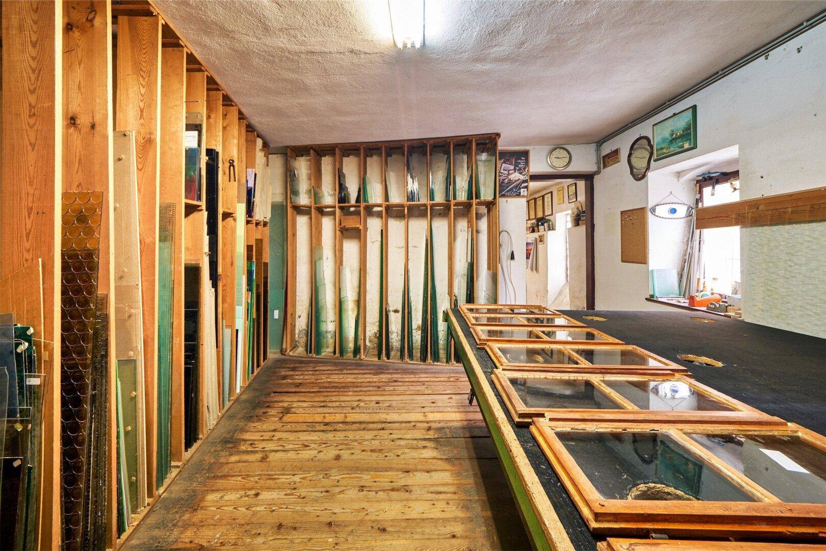 Werkstattraum mit Holzfußboden, Lagerung für Glasplatten und vorbereiteten Fensterrahmen auf einem Tisch.