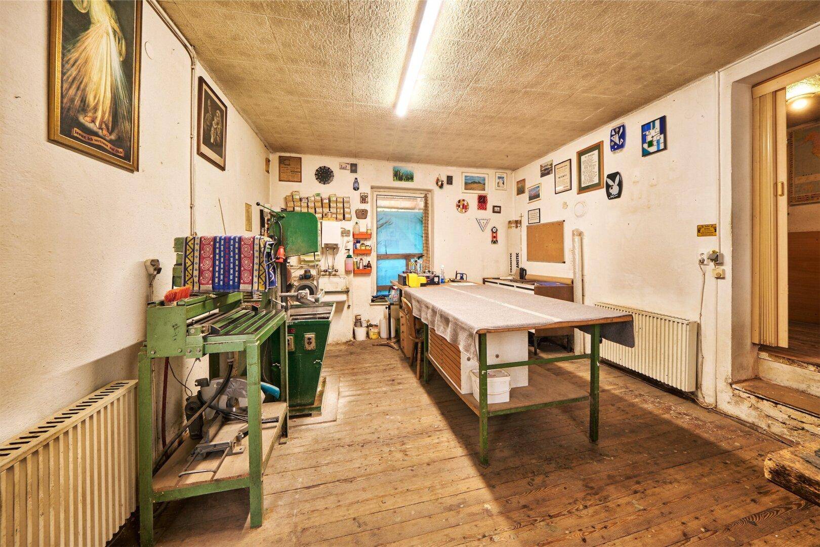 Werkstattraum mit Holzfußboden, Arbeitsmaschinen, einem großen Arbeitstisch und Heizkörpern.